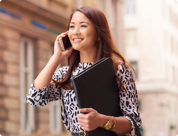 Woman smiling with notebook in hand while she talks on a cell phone outside
