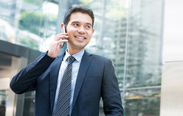 Man smiling outside in front of office building while he talks on the phone