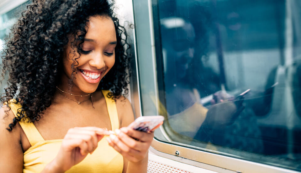 Woman smiling looking down at her phone while standing on train