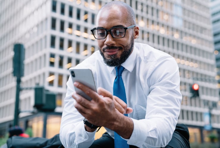 Young business professional looking down at is phone with busy city backdrop