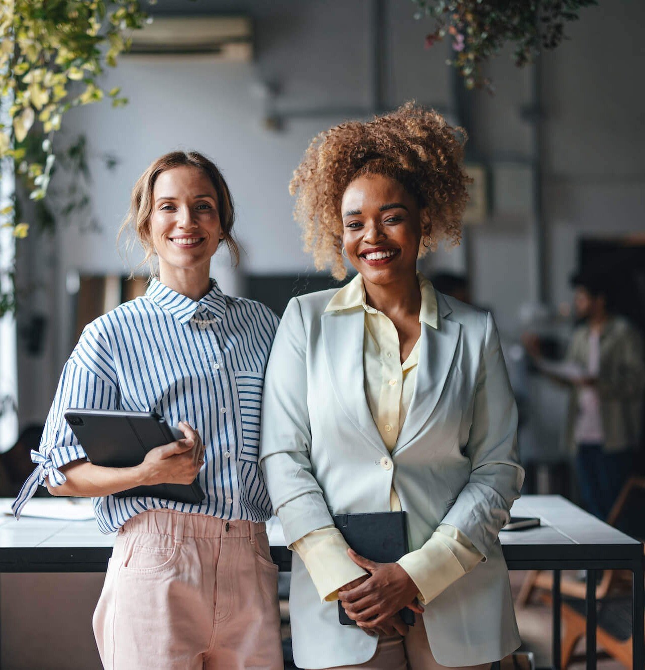 Two Happy Beautiful Blonde Businesswomen Looking At Camera While Standing In The Office