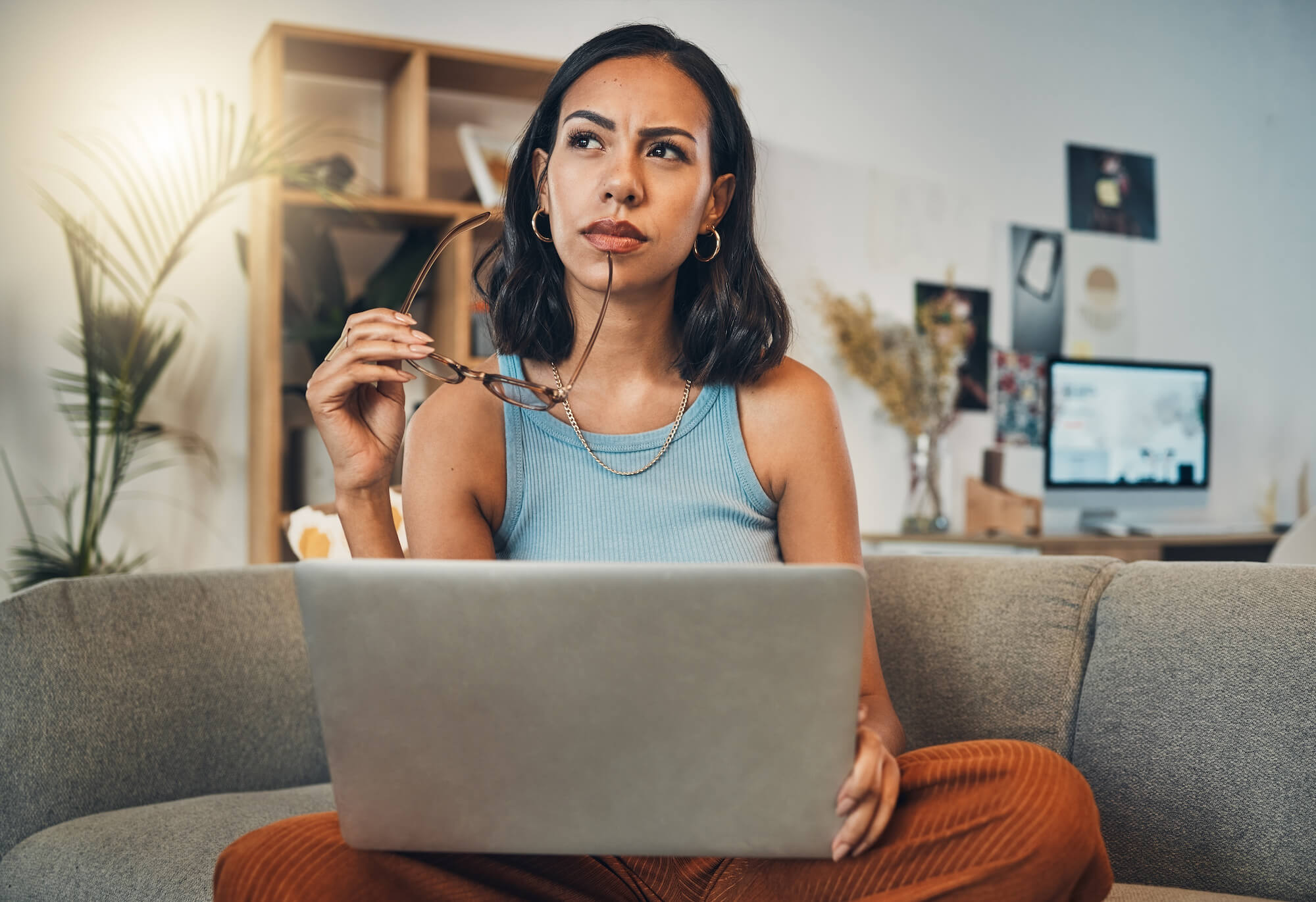 Woman thinking while using laptop for blogging in living room at home