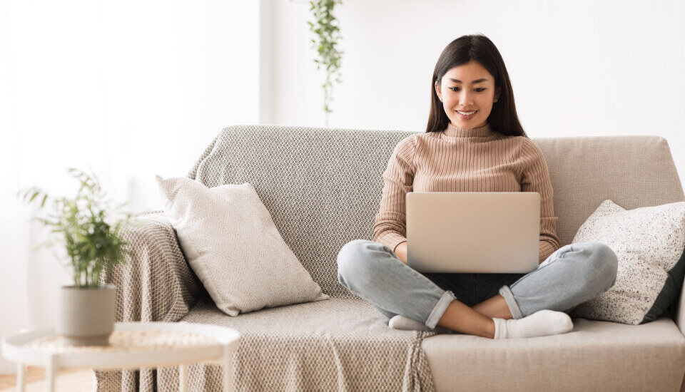 Woman smiling down at her laptop while sitting on a couch at home